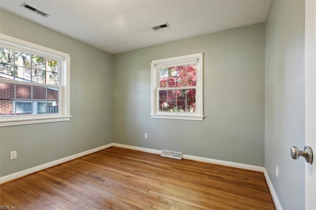 empty room with wood finished floors, visible vents, and plenty of natural light