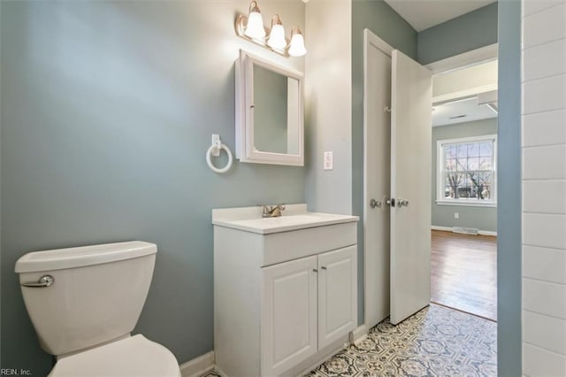 half bath featuring toilet, vanity, visible vents, and baseboards