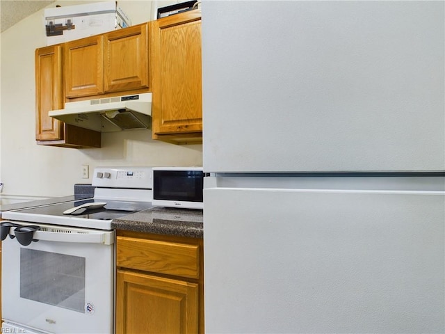 kitchen with dark countertops, white appliances, under cabinet range hood, and brown cabinets