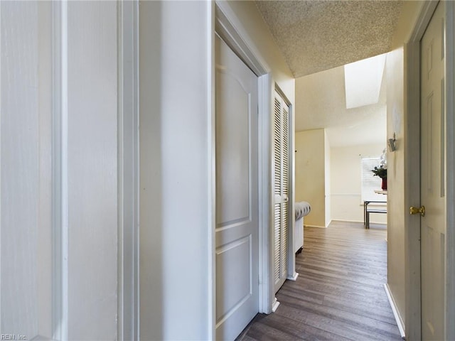 hallway featuring a textured ceiling, baseboards, and dark wood-type flooring