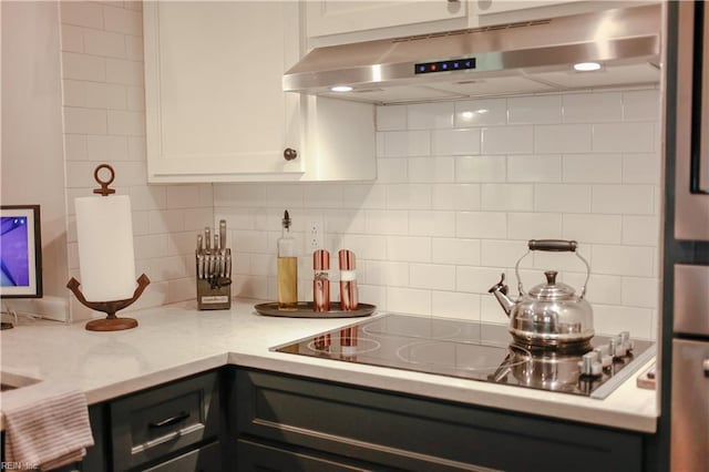 kitchen with light stone counters, black electric stovetop, white cabinetry, backsplash, and under cabinet range hood