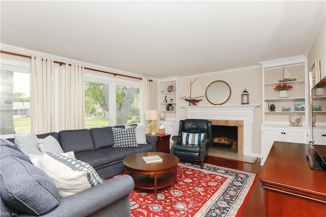living area featuring a tiled fireplace, wood finished floors, built in features, and crown molding