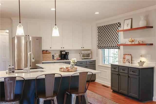kitchen with a kitchen breakfast bar, a sink, freestanding refrigerator, white cabinetry, and wood finished floors