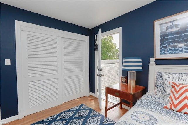 bedroom with baseboards, wood finished floors, a closet, and access to exterior