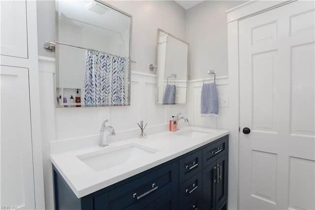 bathroom featuring double vanity, a decorative wall, wainscoting, and a sink