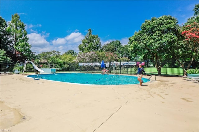 community pool featuring a patio area, a water slide, and fence