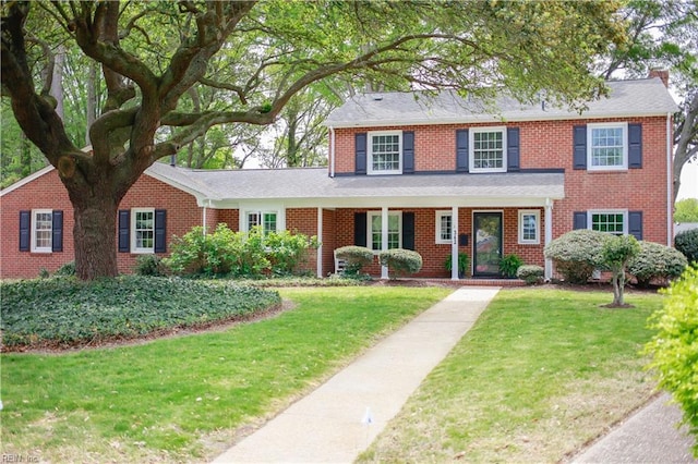 view of front of house with brick siding, a chimney, and a front lawn