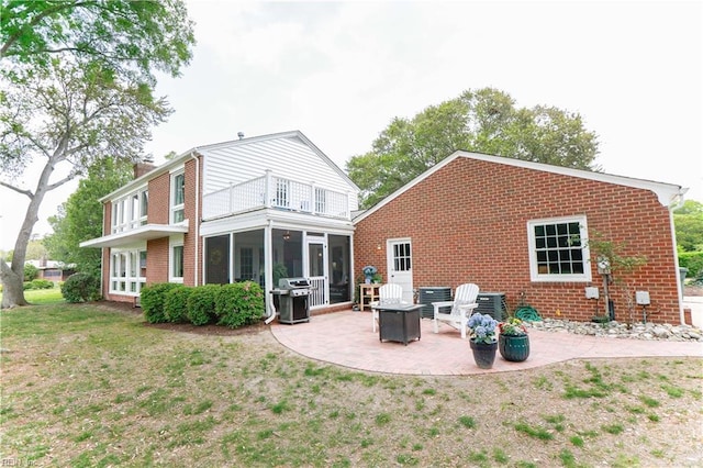 rear view of house with brick siding, a patio area, a balcony, a yard, and a sunroom