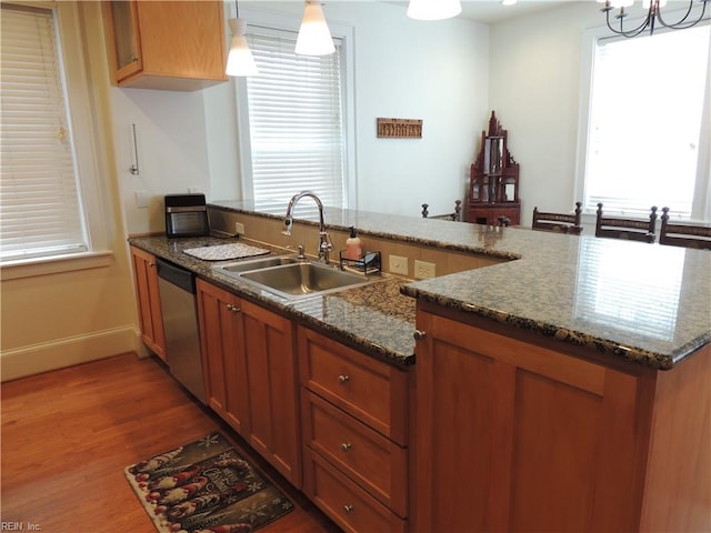 kitchen with stainless steel dishwasher, a sink, plenty of natural light, brown cabinetry, and light wood-type flooring