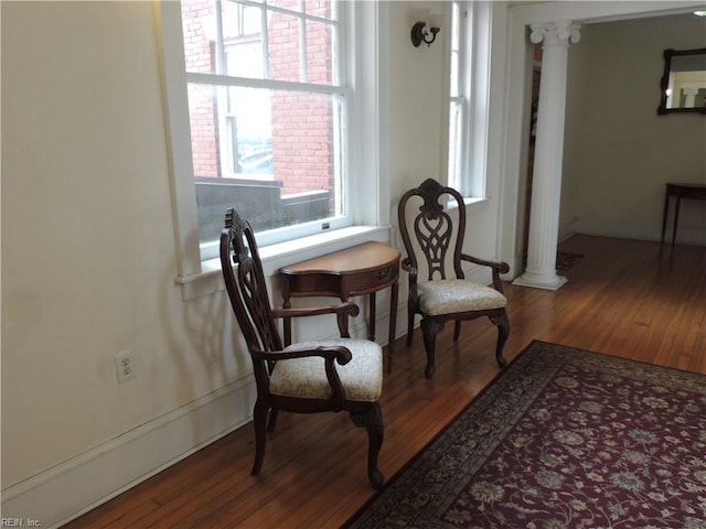 sitting room featuring baseboards, wood finished floors, and ornate columns