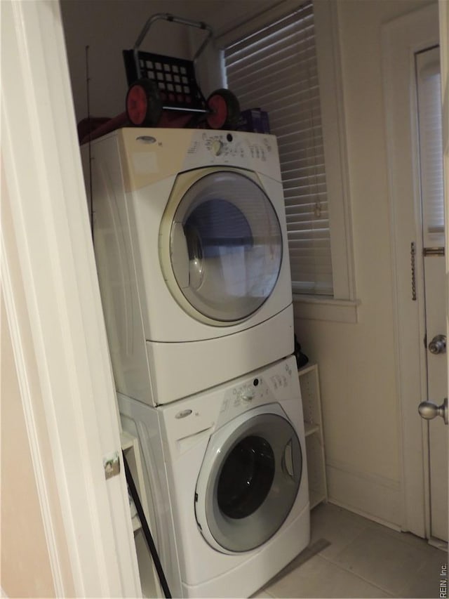 clothes washing area featuring stacked washer and clothes dryer, laundry area, and light tile patterned floors