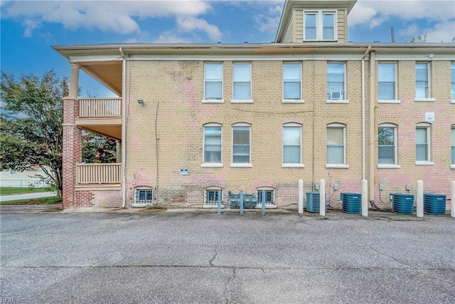 view of side of property featuring cooling unit, a balcony, and brick siding