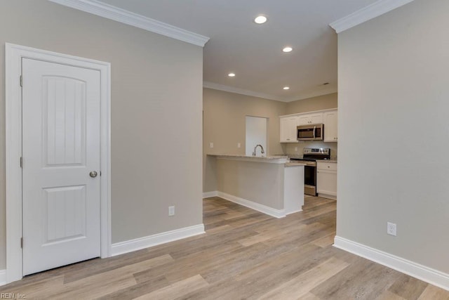 kitchen with light wood-style floors, appliances with stainless steel finishes, white cabinetry, a peninsula, and ornamental molding