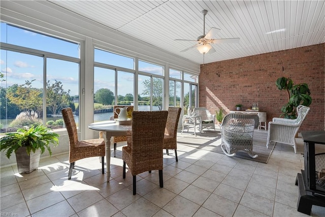 sunroom featuring tile patterned flooring, a water view, and brick wall