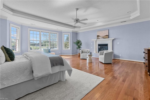 bedroom with a glass covered fireplace, a tray ceiling, a textured ceiling, and wood finished floors