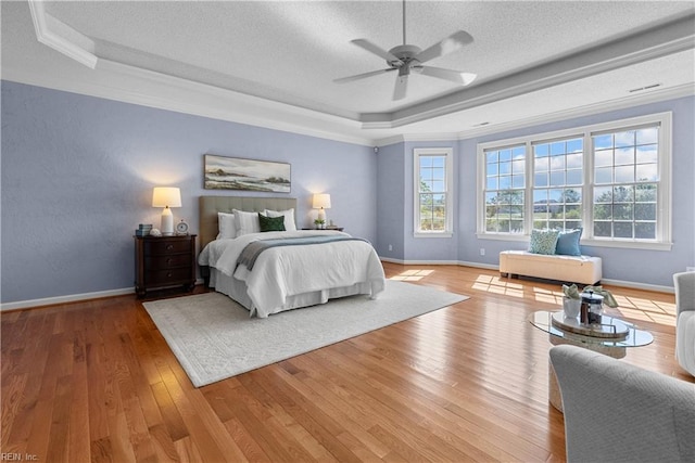 bedroom with ornamental molding, wood finished floors, baseboards, a textured ceiling, and a raised ceiling