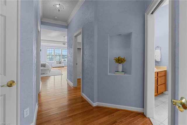 hallway featuring ornamental molding, a textured wall, wood finished floors, baseboards, and a textured ceiling