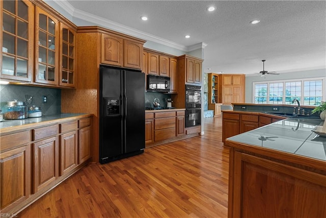 kitchen with a sink, ornamental molding, wood finished floors, and black appliances