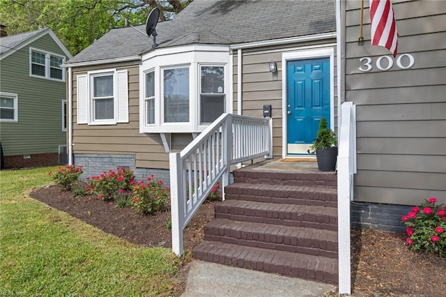 entrance to property featuring a lawn, a shingled roof, and central AC unit