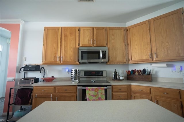 kitchen featuring stainless steel appliances, light countertops, and brown cabinetry