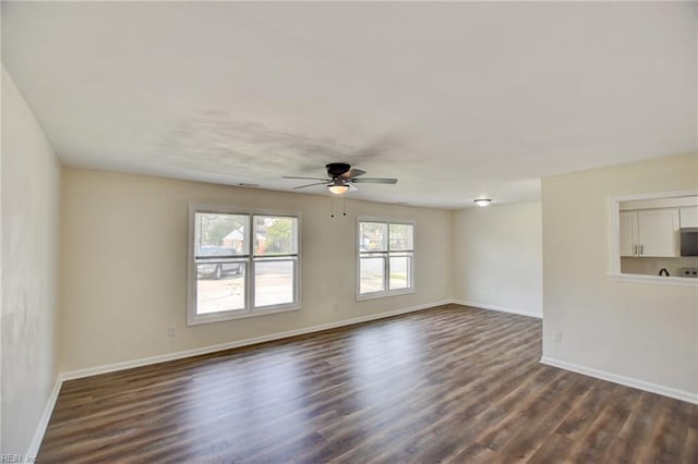 empty room with dark wood-style floors, a ceiling fan, and baseboards