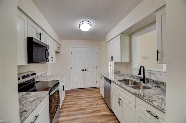 kitchen with light stone counters, light wood-style floors, appliances with stainless steel finishes, and a sink