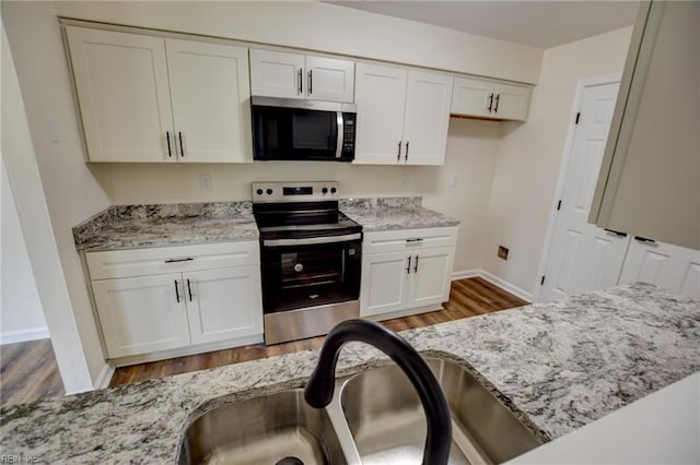 kitchen with a sink, stainless steel appliances, light stone counters, white cabinetry, and wood finished floors