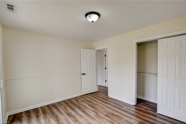 unfurnished bedroom featuring baseboards, visible vents, wood finished floors, and a closet