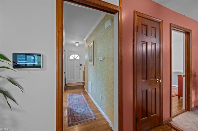 hall featuring visible vents, light wood-style flooring, baseboards, and ornamental molding