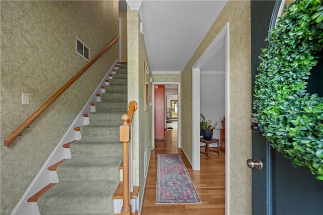 stairs featuring wallpapered walls, wood finished floors, visible vents, and crown molding