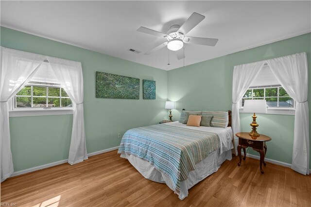 bedroom with baseboards, wood finished floors, multiple windows, and visible vents