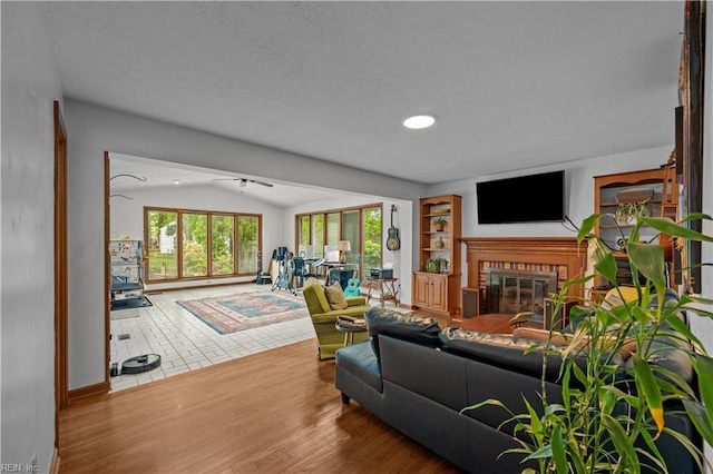 living area with vaulted ceiling, a ceiling fan, wood finished floors, a textured ceiling, and a brick fireplace