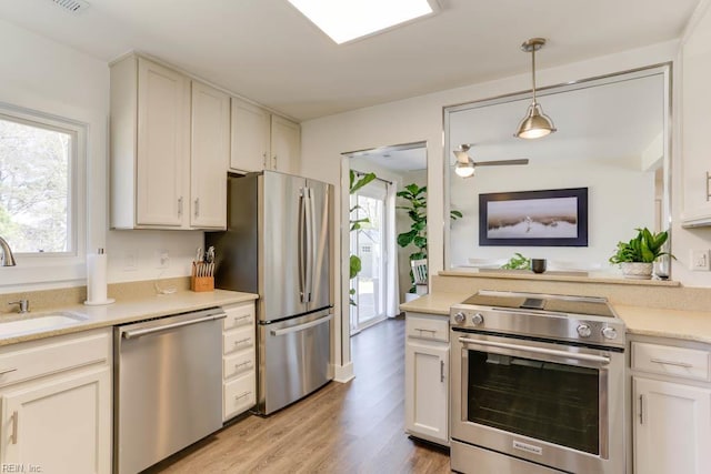 kitchen with light wood finished floors, stainless steel appliances, light countertops, a sink, and decorative light fixtures