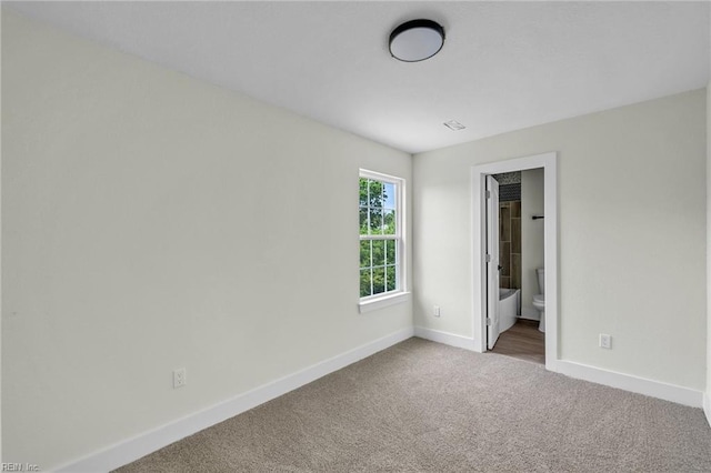 unfurnished bedroom with ensuite bathroom, baseboards, and carpet floors