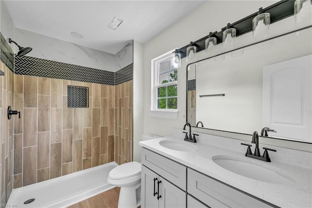 bathroom featuring a tile shower, toilet, a sink, and double vanity