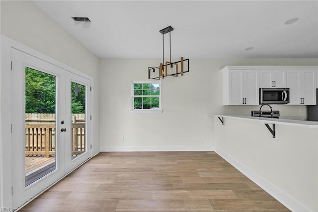 kitchen with white cabinets, light wood-type flooring, light countertops, stainless steel microwave, and baseboards