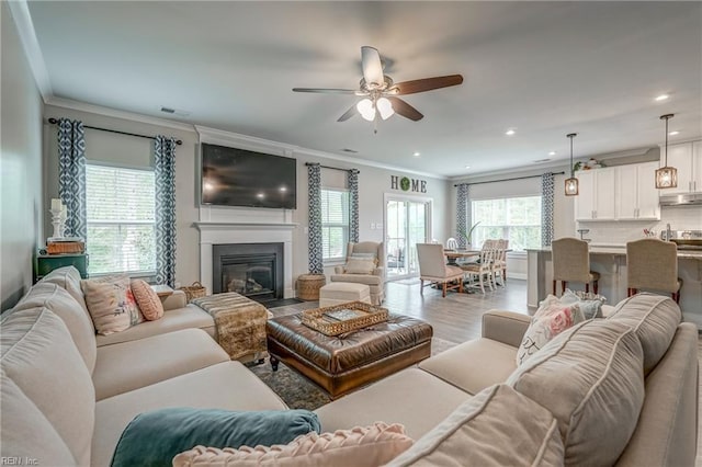 living room with a fireplace with flush hearth, a ceiling fan, crown molding, and recessed lighting