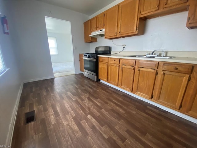 kitchen featuring dark wood finished floors, stainless steel gas stove, under cabinet range hood, light countertops, and a sink