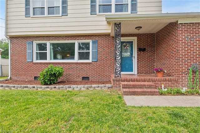 view of exterior entry featuring a lawn, brick siding, and crawl space
