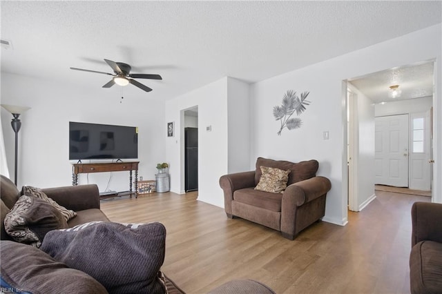 living room with baseboards, wood finished floors, ceiling fan, and a textured ceiling