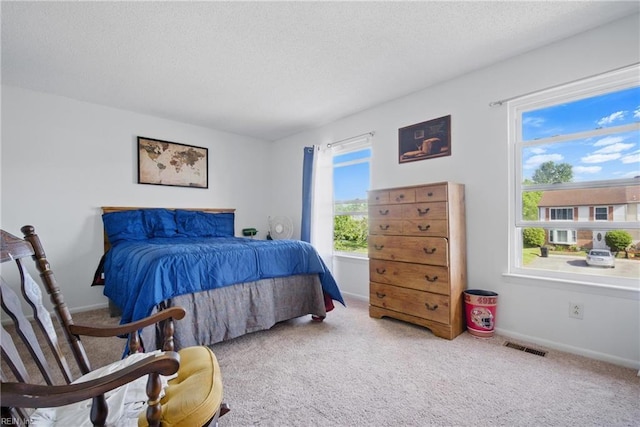 bedroom with a textured ceiling, visible vents, carpet flooring, and baseboards