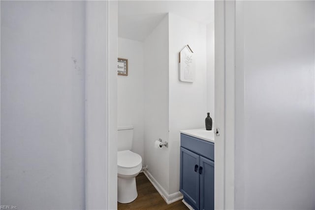 half bathroom with baseboards, wood finished floors, toilet, and vanity