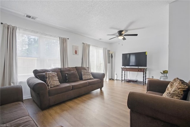 living room featuring visible vents, wood finished floors, a ceiling fan, and a textured ceiling