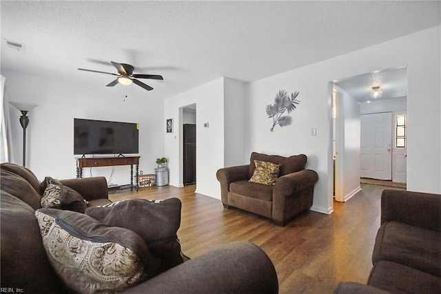 living area featuring wood finished floors, ceiling fan, baseboards, visible vents, and a textured ceiling