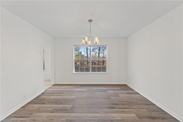 unfurnished dining area featuring baseboards, wood finished floors, and an inviting chandelier