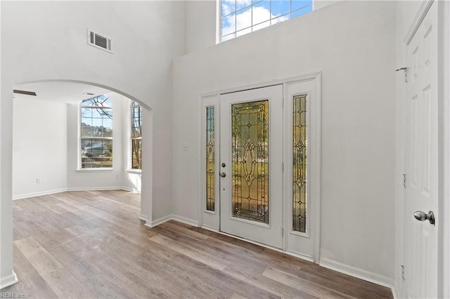 entrance foyer with arched walkways, a towering ceiling, wood finished floors, and visible vents