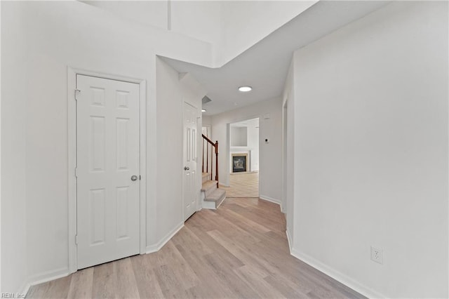 hallway with stairs, light wood finished floors, and baseboards