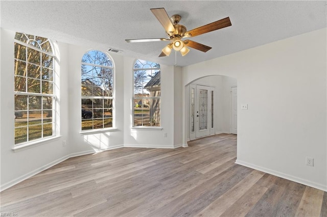 unfurnished room featuring wood finished floors, visible vents, a ceiling fan, arched walkways, and a textured ceiling