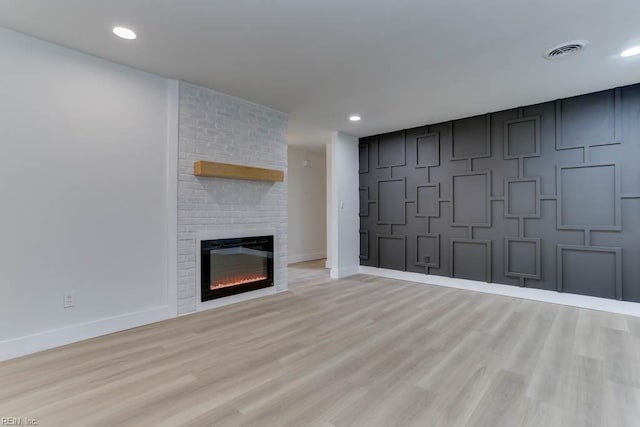 unfurnished living room featuring a brick fireplace, light wood-style flooring, visible vents, and baseboards