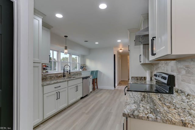 kitchen featuring light wood finished floors, exhaust hood, backsplash, a sink, and appliances with stainless steel finishes